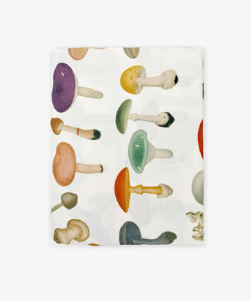 The John Derian Fungi Tablecloth is a folded white cloth adorned with a vibrant vintage-inspired mushroom pattern scattered across its surface.