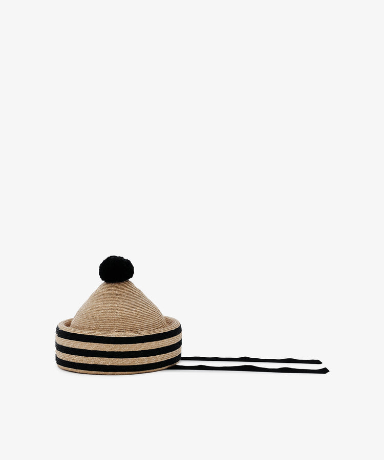 The Circus Hat is a natural straw hat with a striped crown, black pompom on top, and two long black ties on the sides.