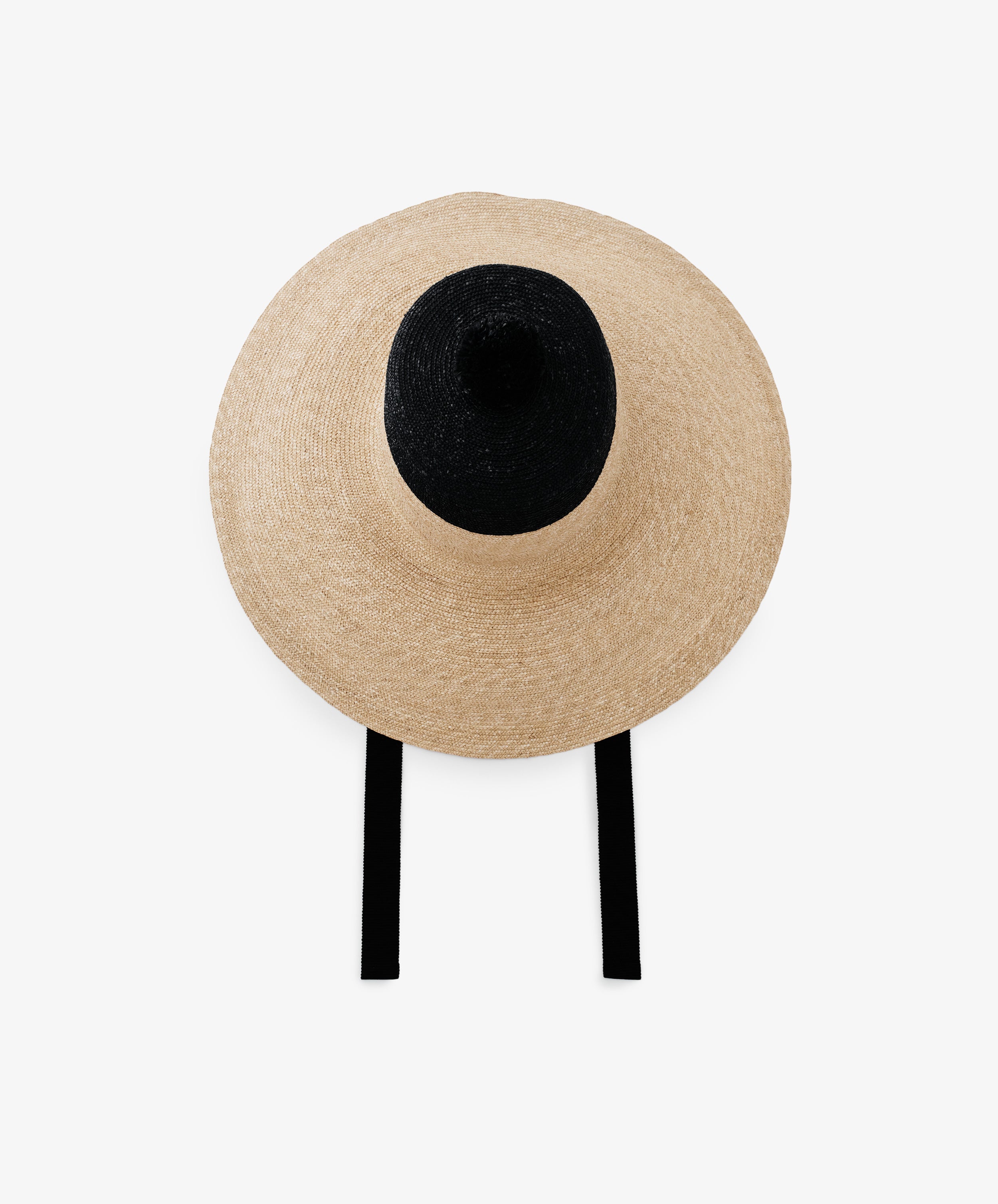 The Dahlia Hat is a handwoven straw hat with a dramatic wide brim, black crown, and elegant black ties, shown from above on a plain white background.
