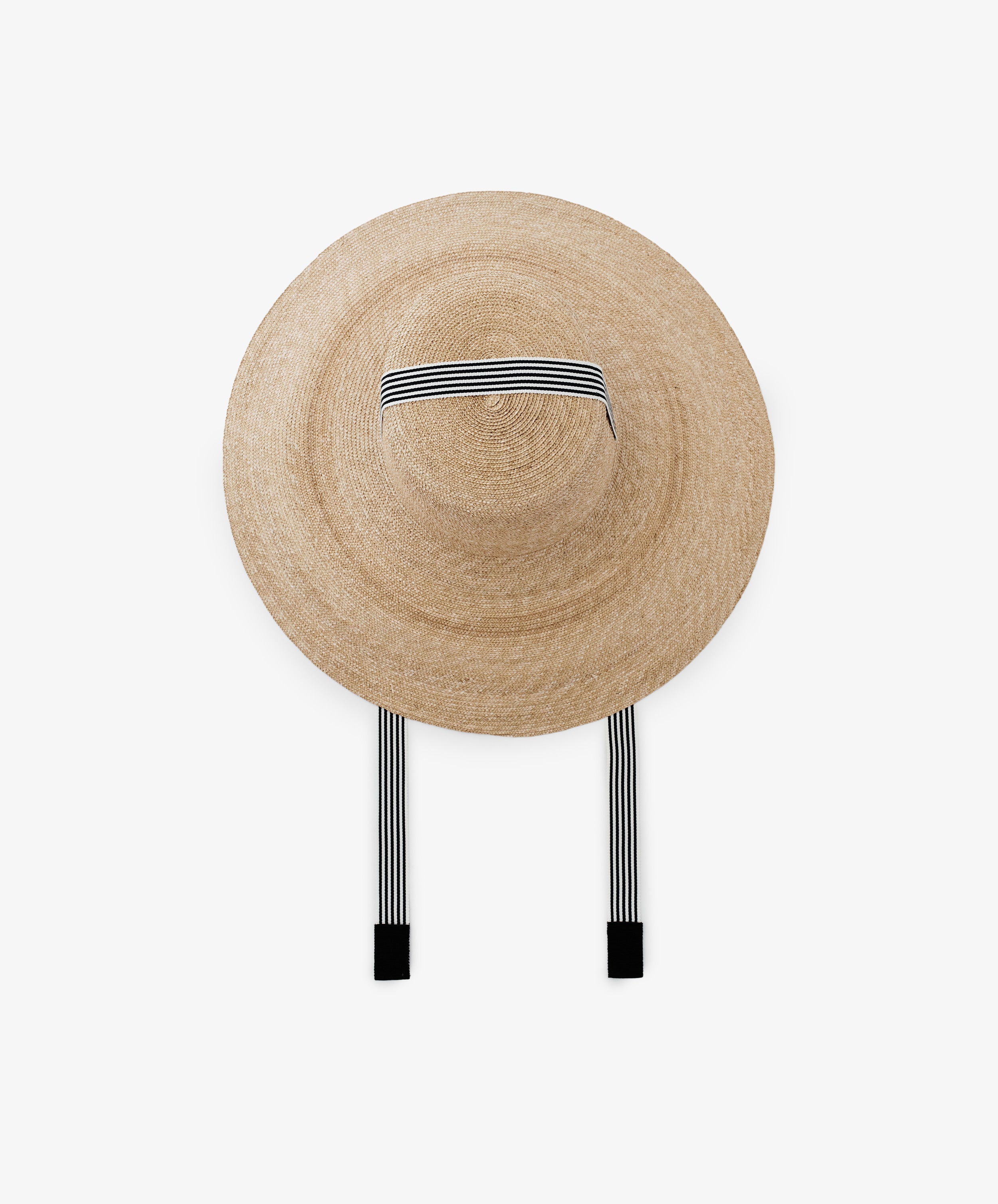 The Dahlia Hat is a natural straw wide-brim hat featuring black and white striped ribbons, shown on a plain white background.