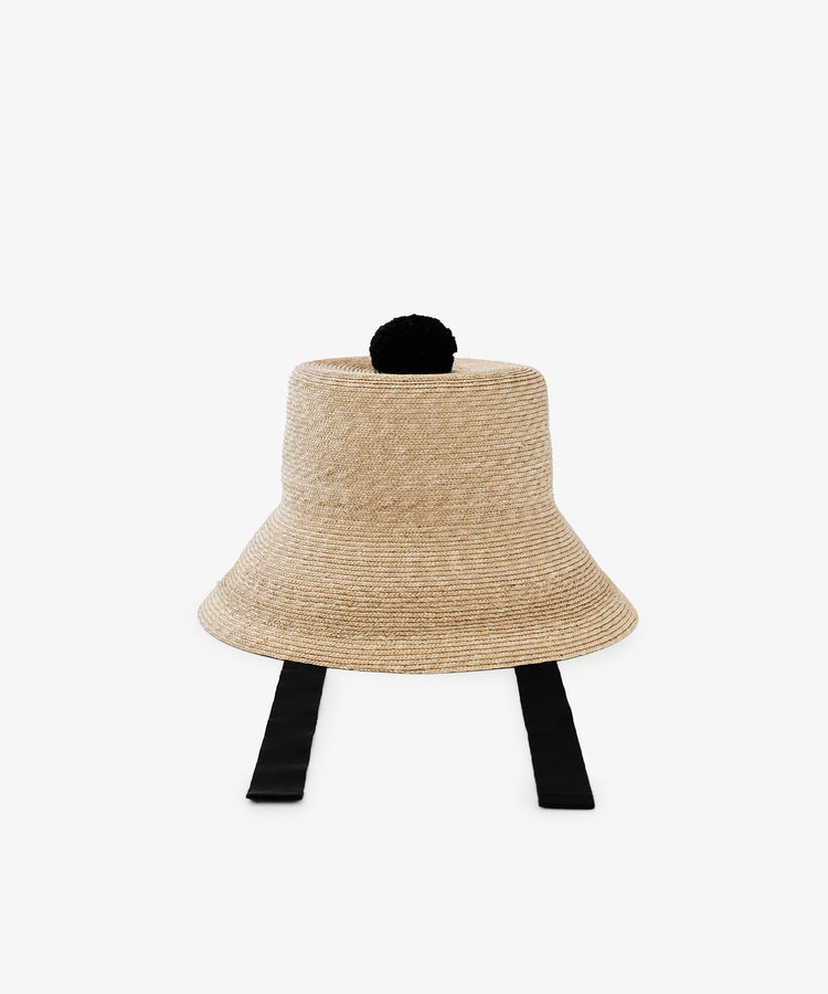 The Mount Hat is a beige handwoven straw hat featuring a wide brim, black ribbon ties, and a black pom-pom on top, shown against a plain white background.