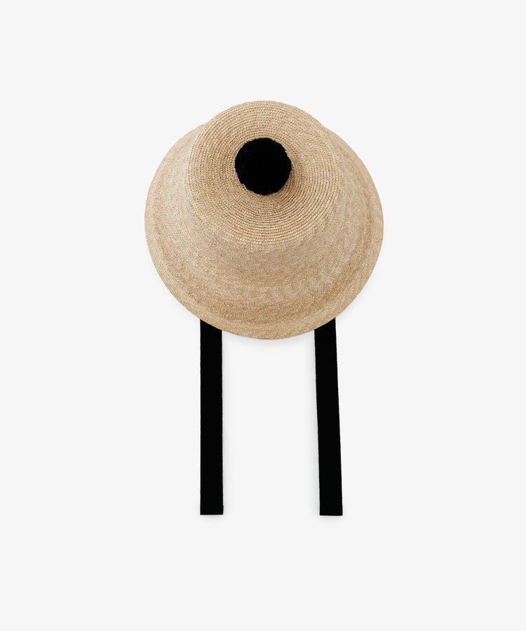 The Mount Hat is a beige handwoven straw hat featuring a black pom-pom on top and two black straps, shown against a plain white background.