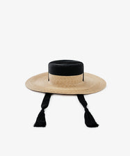 The Treaty Hat features a wide brim, flat crown, black band detail, and two black tasseled chin straps—ideal for adding resort glamour.