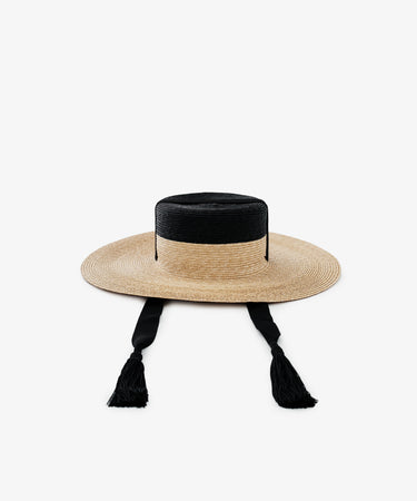 The Treaty Hat features a wide brim, flat crown, black band detail, and two black tasseled chin straps—ideal for adding resort glamour.
