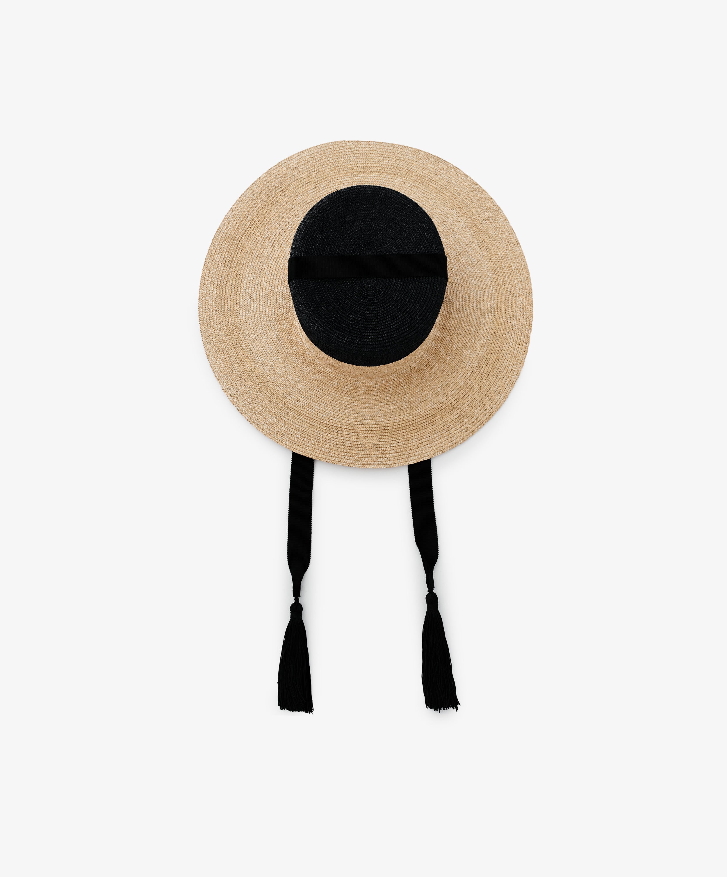 The Treaty Hat features a round straw design, wide brim, black crown with a ribbon, and two long black tassels, offering resort glamour.