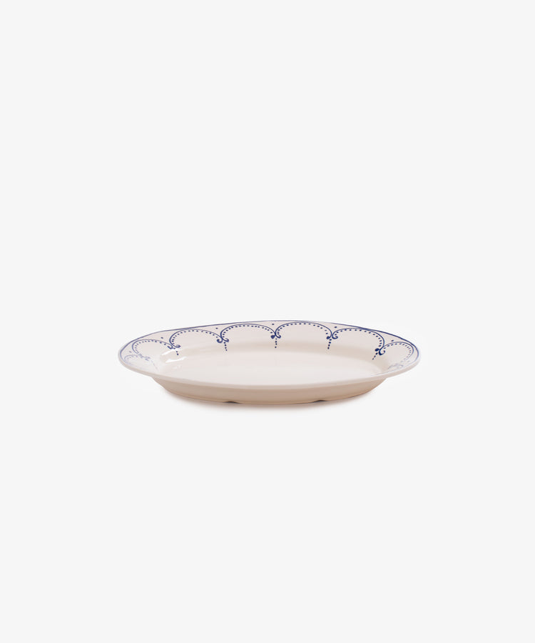 The Arco Oval Serving Platter features a shallow ceramic design with a white base and blue scalloped rim, inspired by traditional Portuguese patterns, shown against a plain white background.