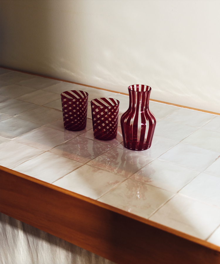 Two red striped glasses sit beside carafe on white tiled counter.