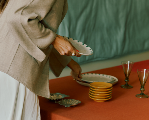 Person arranging ceramic plates on a table with a green curtain in the background