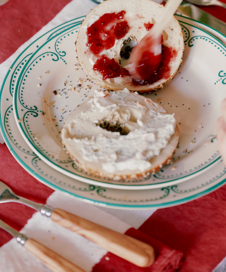 A Vito Dinner Plate, part of a set of 4, holds a bagel—one half with cream cheese, the other with red jam. Two wood-handled utensils rest beside it, ideal for everyday use.