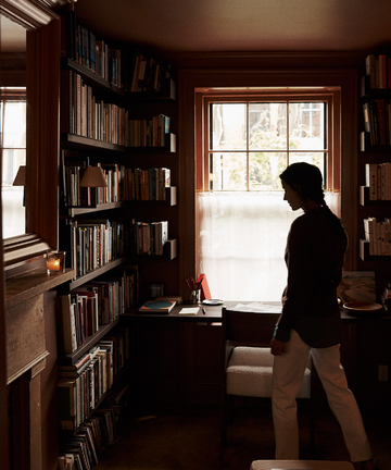 Person standing in a dimly lit room with bookshelves and a window