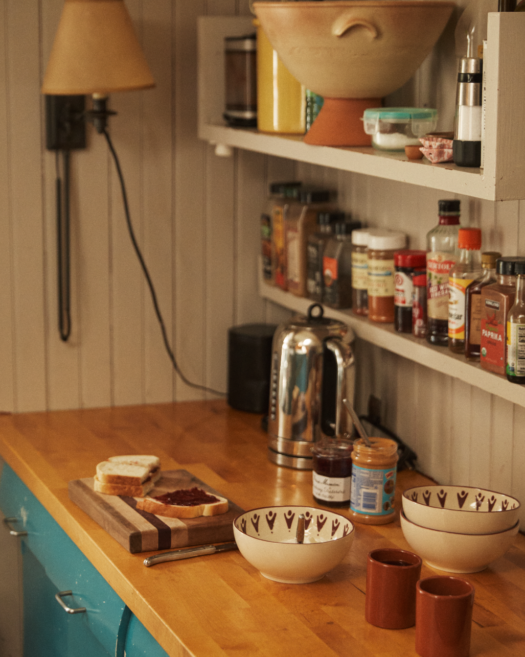 A kitchen counter with a cutting board, bread with jam, Vito Cereal Bowls (set of 4), mugs, a kettle, and shelves holding spices and condiments—perfect for everyday use.