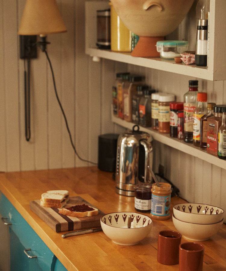 A kitchen counter with a cutting board, bread with jam, Vito Cereal Bowls (set of 4), mugs, a kettle, and shelves holding spices and condiments—perfect for everyday use.