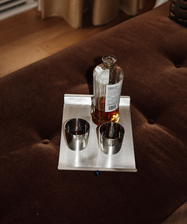 The Alexander Stemless Tumbler Set of 2 sits on a rectangular tray with a bottle of liquor atop a brown cushioned surface, lending a modern touch to the tableware arrangement.