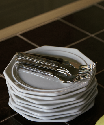 A stack of Cirrus Scalloped Plates rests on a dark tiled surface, with silverware neatly arranged on top.