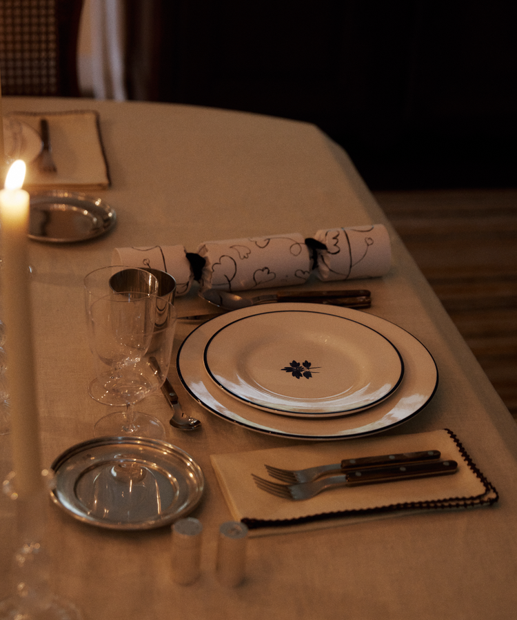 Elegant table setting featuring the Beatrix Salad Plate, Set of 4, with cutlery, glass, napkin, paper cracker, candle, and silver tray on a beige tablecloth.