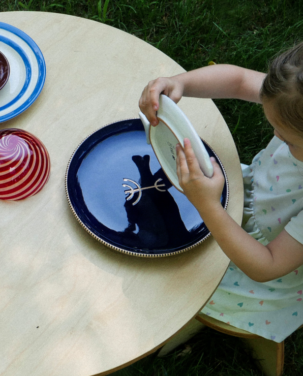 little girl playing with plates on a wood table outside