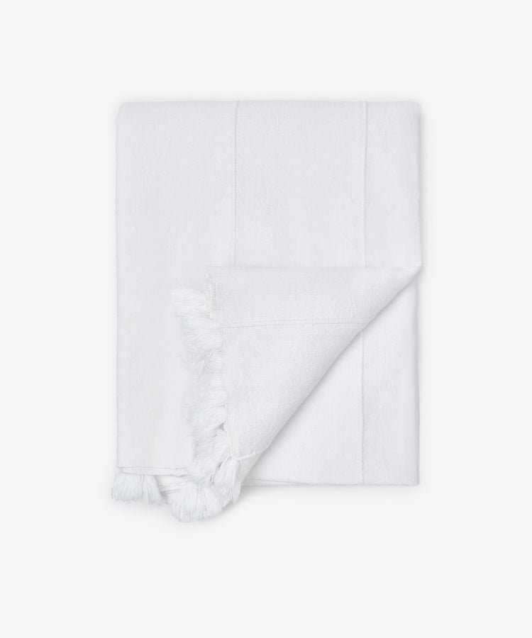 The Cordon Tablecloth is shown folded against a plain white background, featuring subtle stripes, soft cotton texture, and fringe on two edges.