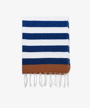 The La Plage Towel is a versatile beach towel featuring neat horizontal navy blue and white stripes, a brown band at one end, and white fringe tassels.