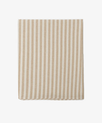 The Martin Striped Tablecloth features classic beige and white stripes inspired by English ticking, displayed neatly folded on a white background.
