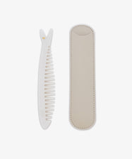 The Capri Sardine Comb, a white detangling comb with a textured handle, is shown beside its beige stitched leather protective case on a white background.