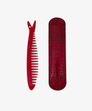 The Capri Sardine Comb, featuring a small star near the top, is placed beside a textured red case on a white background.