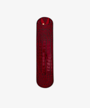 The Capri Sardine Comb is shown on a plain white background in a sleek, narrow red leather crocodile-textured case with rounded ends and a gold accent, perfect for storing your favorite tortoiseshell comb.