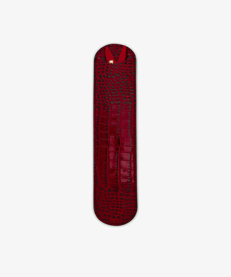 The Capri Sardine Comb is shown on a plain white background in a sleek, narrow red leather crocodile-textured case with rounded ends and a gold accent, perfect for storing your favorite tortoiseshell comb.