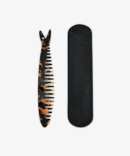 The Capri Sardine Comb, a tortoiseshell comb shaped like a fishbone, is placed beside a black leather case on a white background.