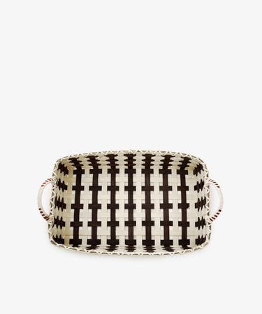 The Folk Fleur Breakfast Tray is a handwoven rectangular reed tray with black and natural-colored stripes, featuring two white handles with red accents on each side—showcasing the timeless charm of rustic basketware.
