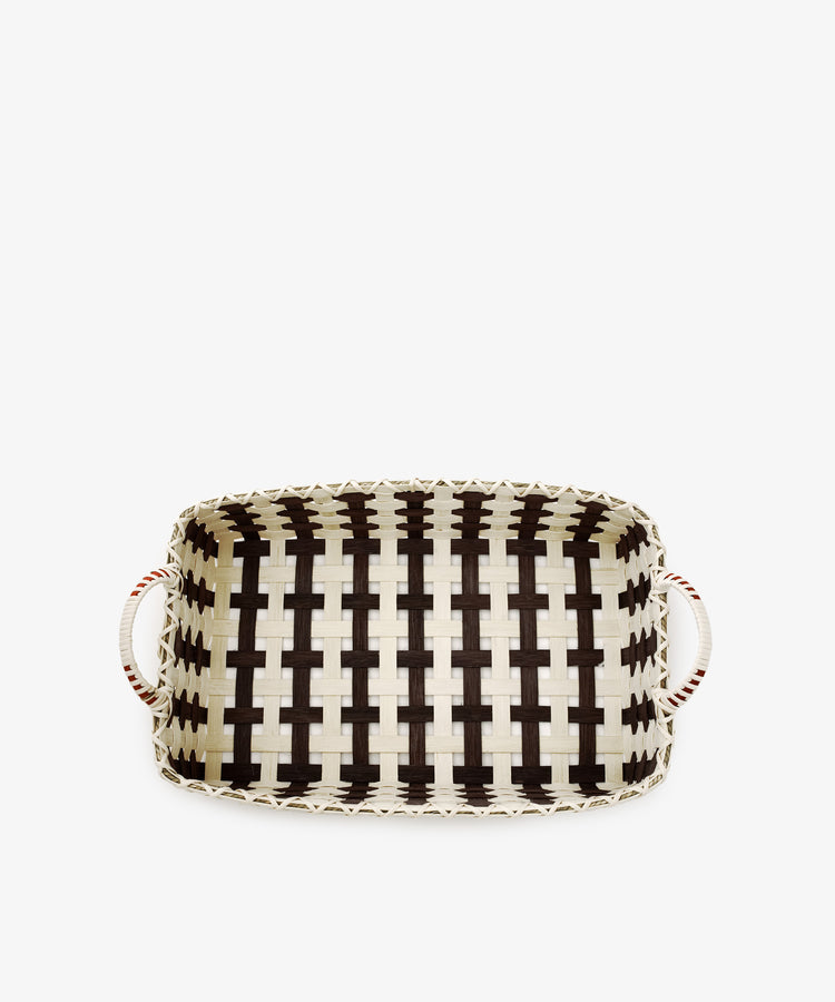 The Folk Fleur Breakfast Tray is a handwoven rectangular reed tray with black and natural-colored stripes, featuring two white handles with red accents on each side—showcasing the timeless charm of rustic basketware.
