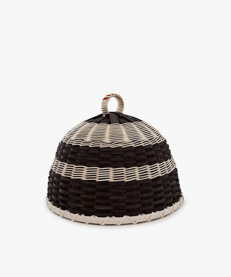Introducing the Folk Fleur Cloche: a handwoven, dome-shaped basket distinguished by alternating black and white horizontal stripes and topped with a convenient loop handle. Designed for both style and practicality, it serves perfectly as a cheese cover for outdoor entertaining. Set against a plain white background, the Folk Fleur Cloche seamlessly combines modern appeal with thoughtful functionality.
