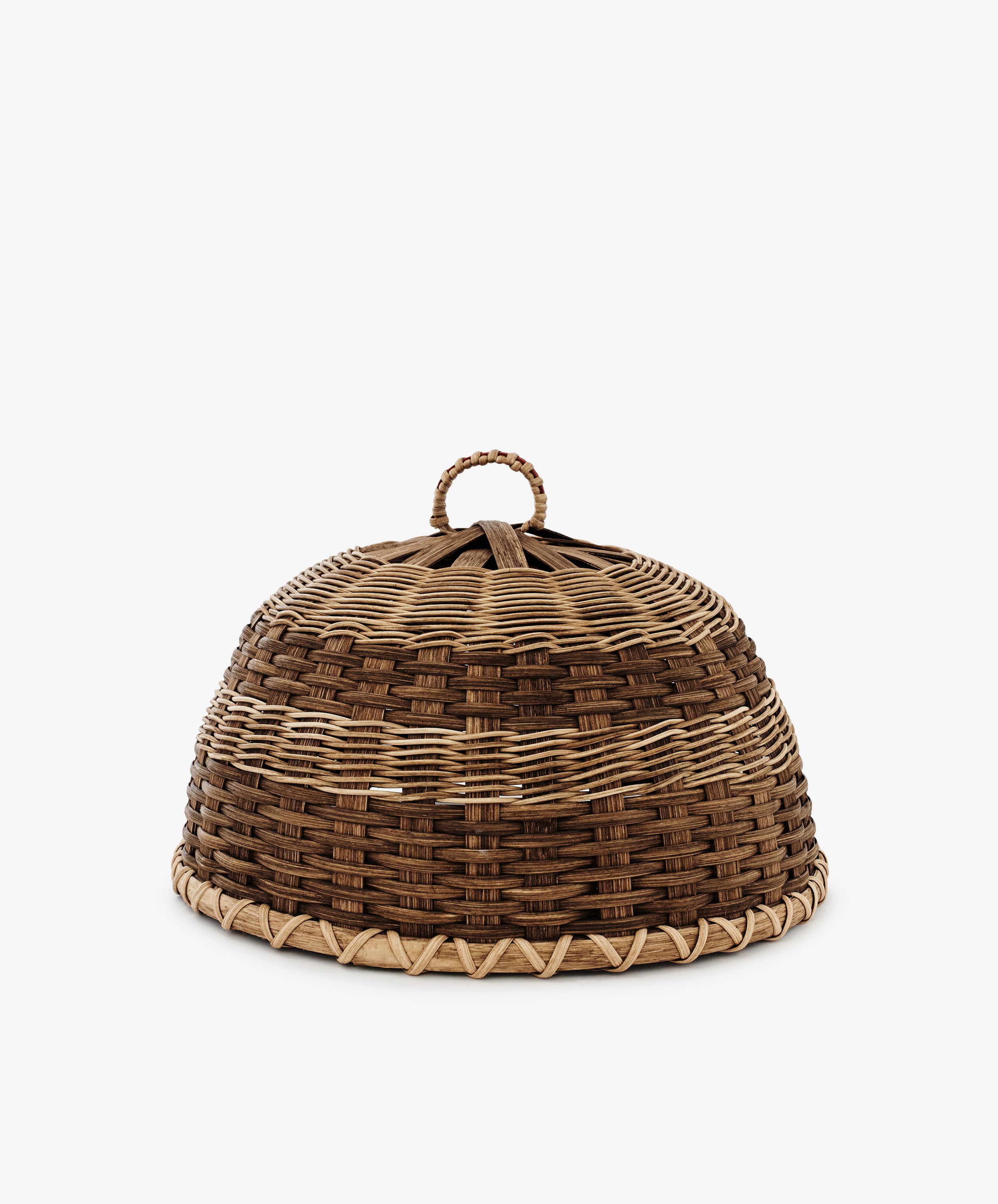 The Folk Fleur Cloche is a dome-shaped, handwoven piece with a wicker top handle and alternating light and dark brown patterns—ideal for stylish outdoor entertaining.