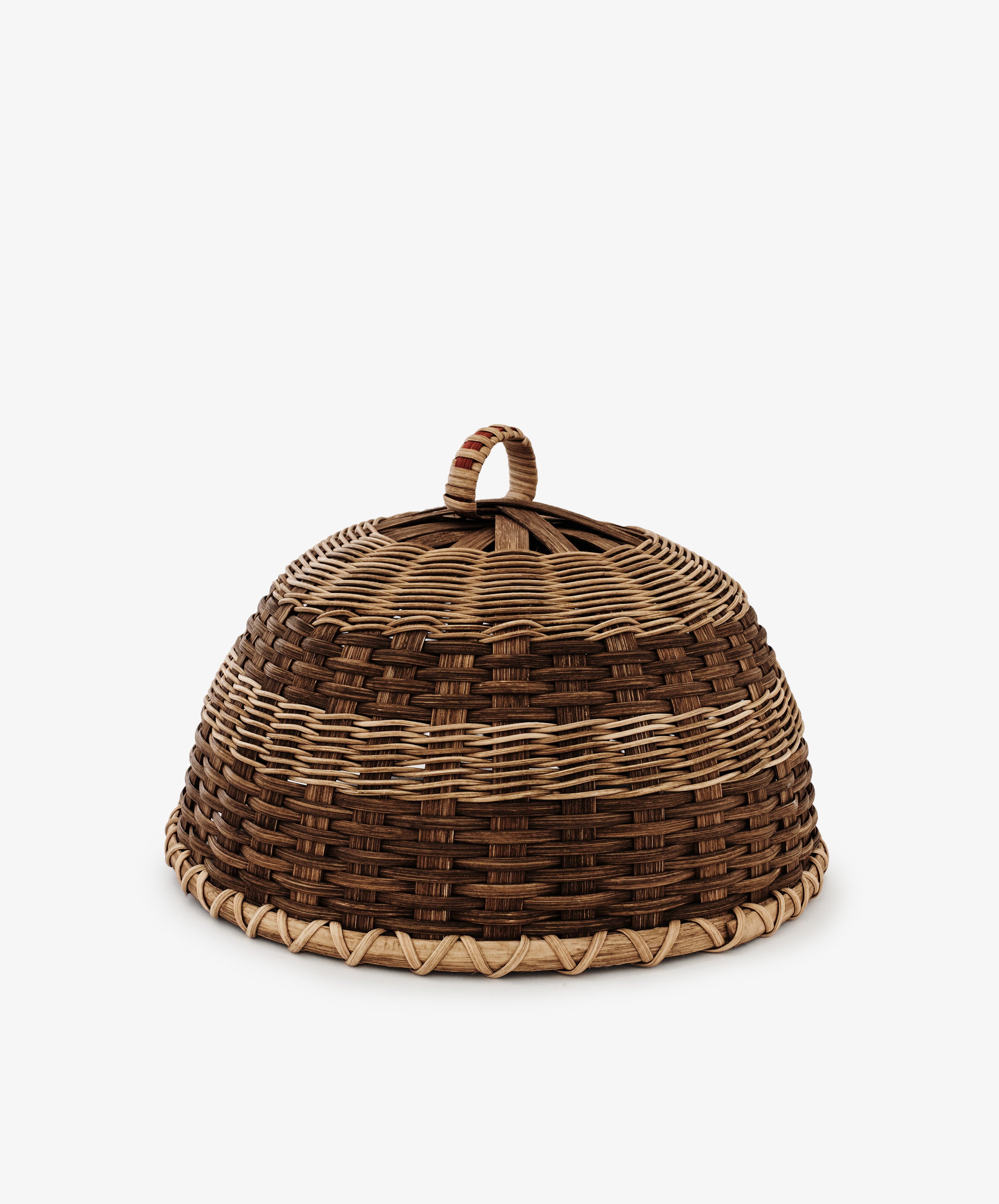 The Folk Fleur Cloche is a dome-shaped, handwoven piece with a top handle and alternating light and dark brown bands—perfect for outdoor entertaining.