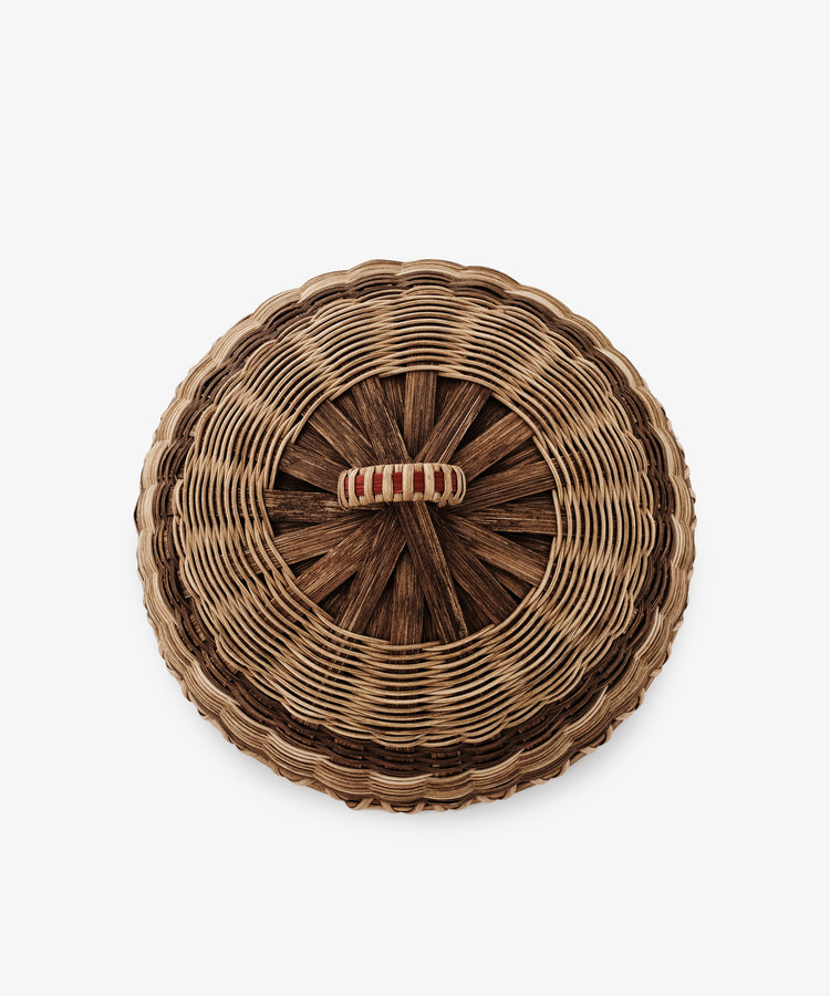 The Folk Fleur Cloche is a round, handwoven basket with a lidded top and a beige-and-red wrapped central handle—ideal for outdoor entertaining. Shown in an overhead photo on a white background.
