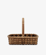 The Folk Fleur Hand Basket, a rectangular rattan basket with an upright handle crafted from natural materials, is displayed against a plain white background.