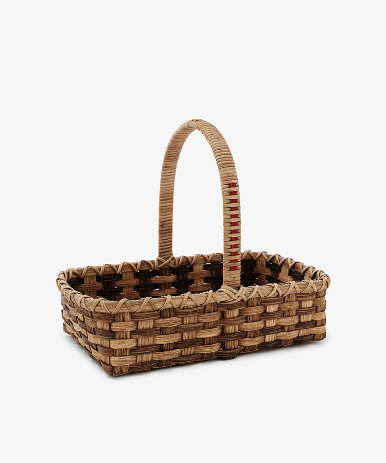 The Folk Fleur Hand Basket is a rectangular rattan basket with a single arched handle, crafted from natural materials and shown on a plain white background.