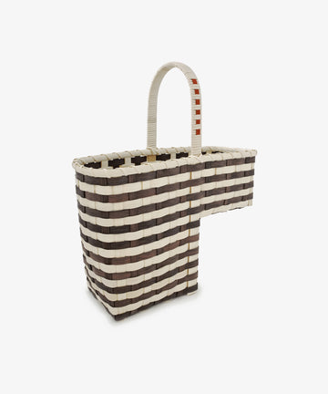 Introducing the Stair Tote: a handwoven rectangular storage basket with bold black and white stripes and a distinctive L-shaped extension crafted specifically for use as a stair basket. It features a single curved handle, wrapped in white with a red accent, for easy transport.