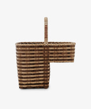 The Stair Tote is a handwoven rattan basket with a unique L-shaped design and single handle, ideal as a stylish staircase organizer. Shown against a plain white background.