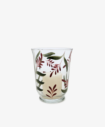 The Botanical Candle Holder features clear glass and a partially melted white candle, adorned with green and burgundy leaves, making it a charming decorative table centerpiece.