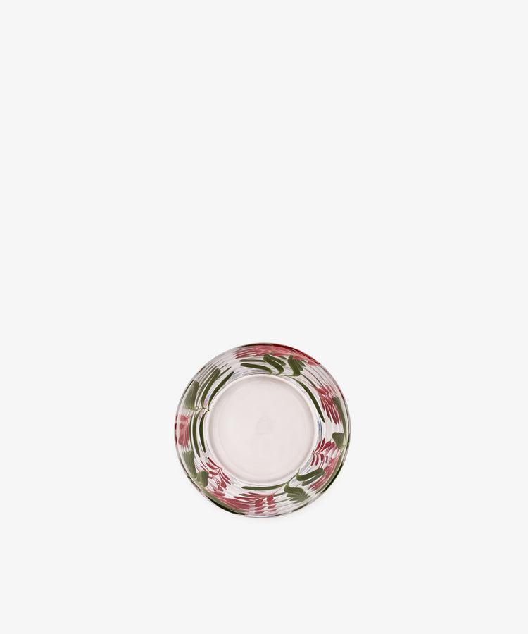 The Botanical Pinch Pot, a round glass plate with a clear center and a border adorned in hand-painted swirls of red, pink, and green, is elegantly photographed against a white background—an exquisite tabletop accoutrement for any setting.