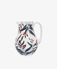 The Botanical Jug is a clear glass pitcher with a white handle, hand painted with blue and red leaf patterns—an elegant and unique piece of tableware.