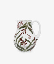 The Botanical Jug is a clear glass pitcher with a handle, featuring hand-painted green leaves and red floral accents—a beautiful example of handmade craftsmanship.