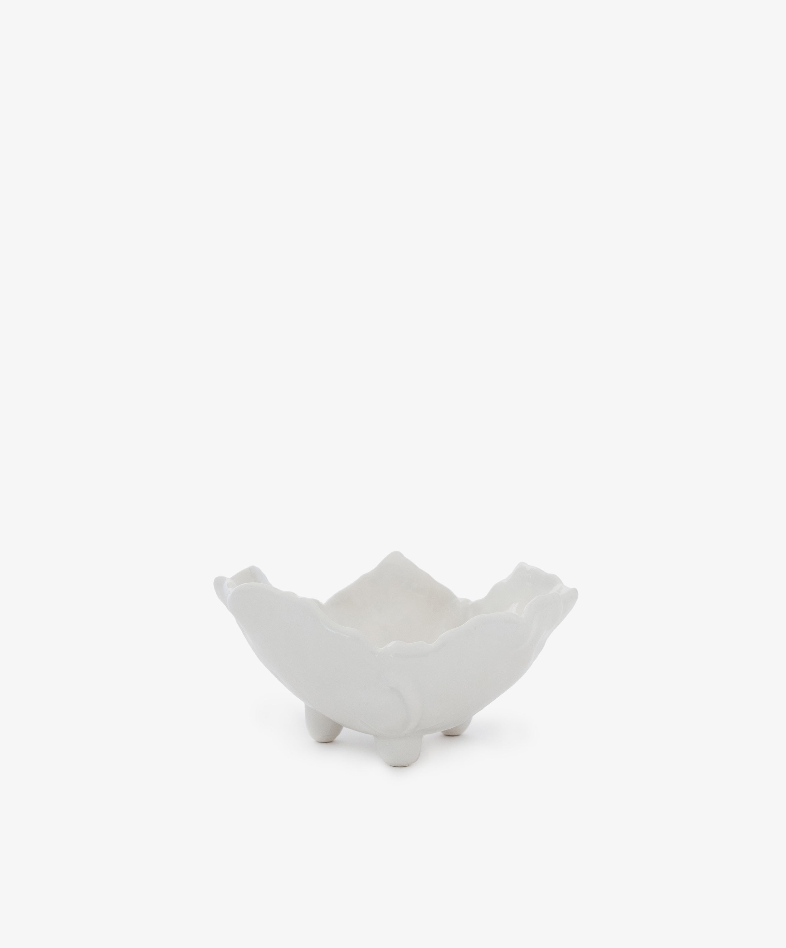 The Leaf Bowl is a white ceramic dish with a wavy, flower-like edge and three small rounded feet, shown on a plain white background. It's a charming piece perfect for display.