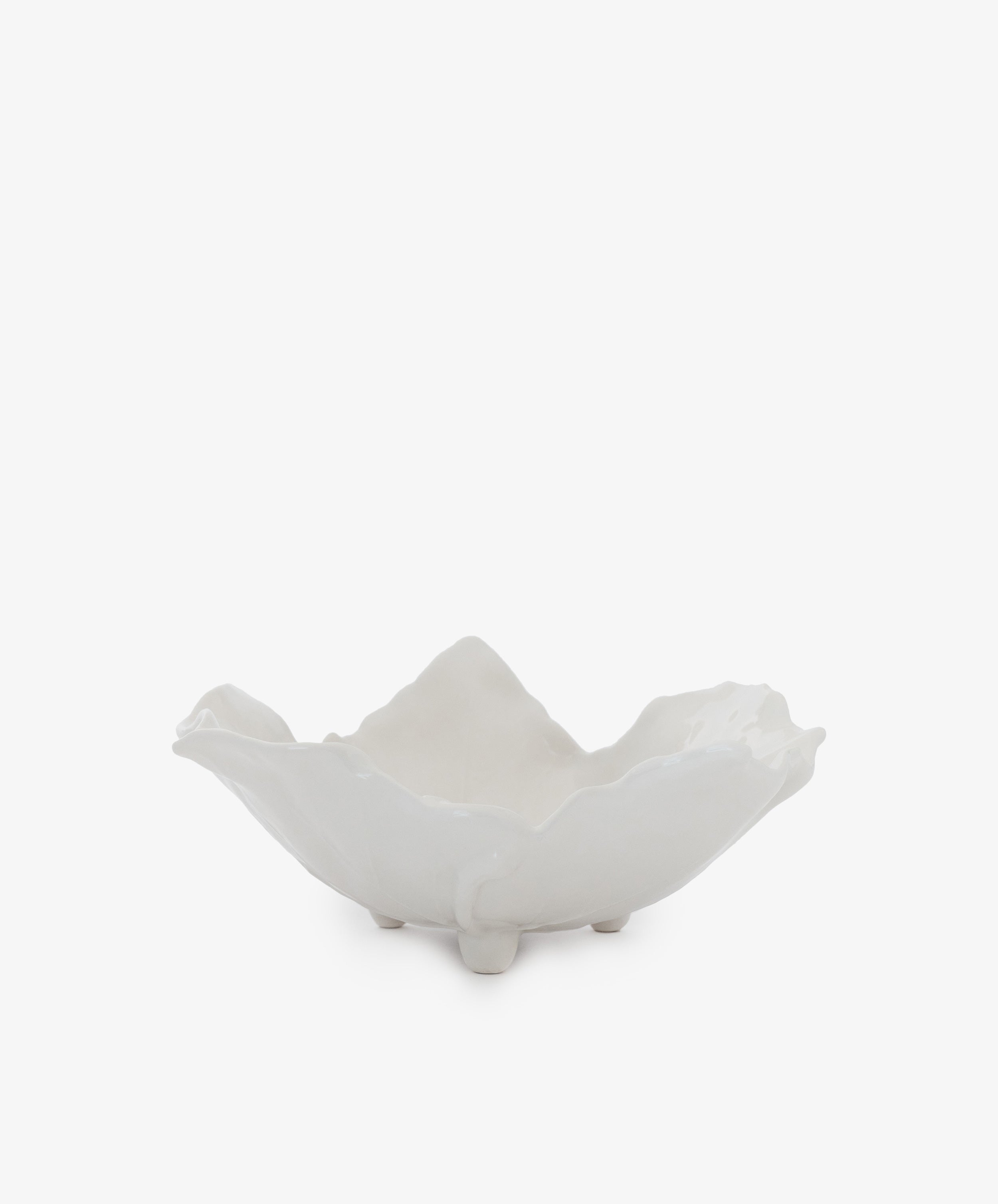 The Leaf Serving Bowl is a white ceramic earthenware piece with an irregular, wavy edge and three small feet, evoking an Italian countryside table. Shown against a plain white background.