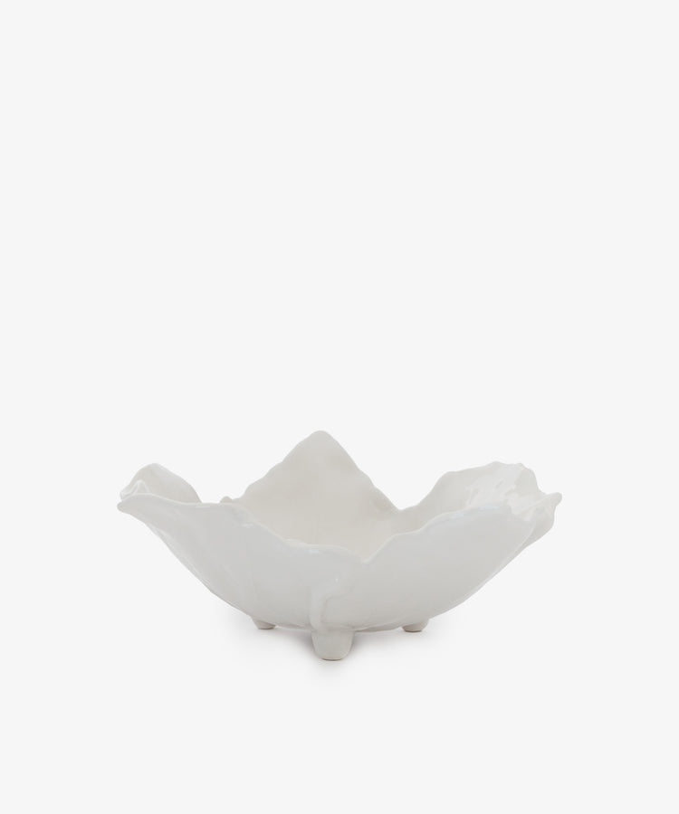 The Leaf Serving Bowl is a white ceramic earthenware piece with an irregular, wavy edge and three small feet, evoking an Italian countryside table. Shown against a plain white background.