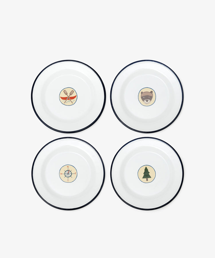 The Camp Plates, Set of 4, features white enamel with black rims and playful illustrations—crossed paddles, bear face, compass, and pine tree—for a vintage scout badge touch to kids’ tableware.