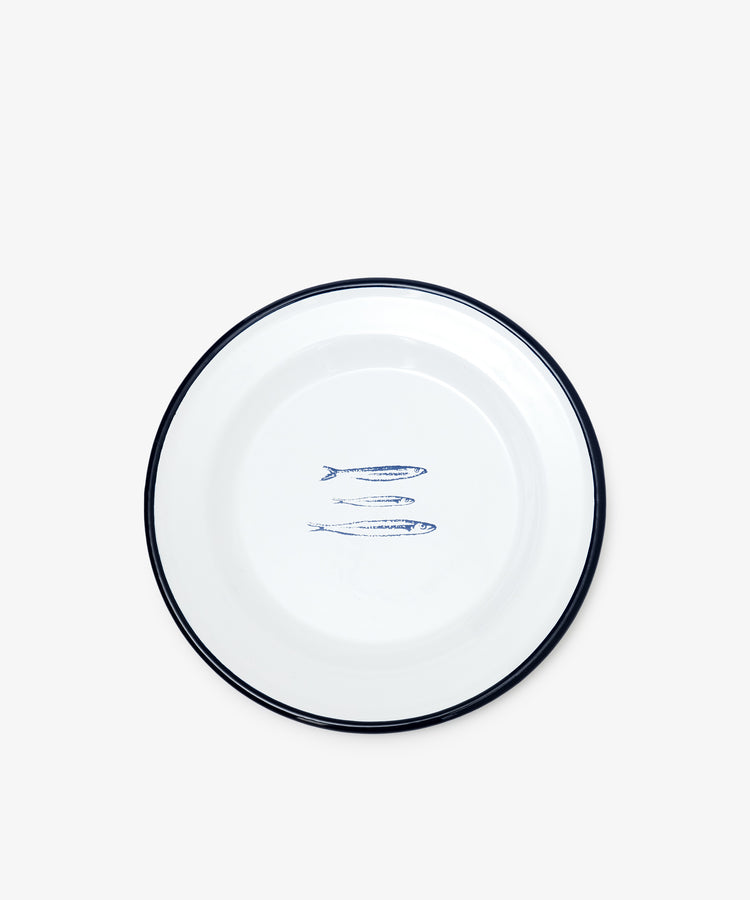 The Il Pesce Enamel Plate, Set of 2, features a white plate with a blue rim and an illustration of three blue sardines in the center, shown against a plain white background.