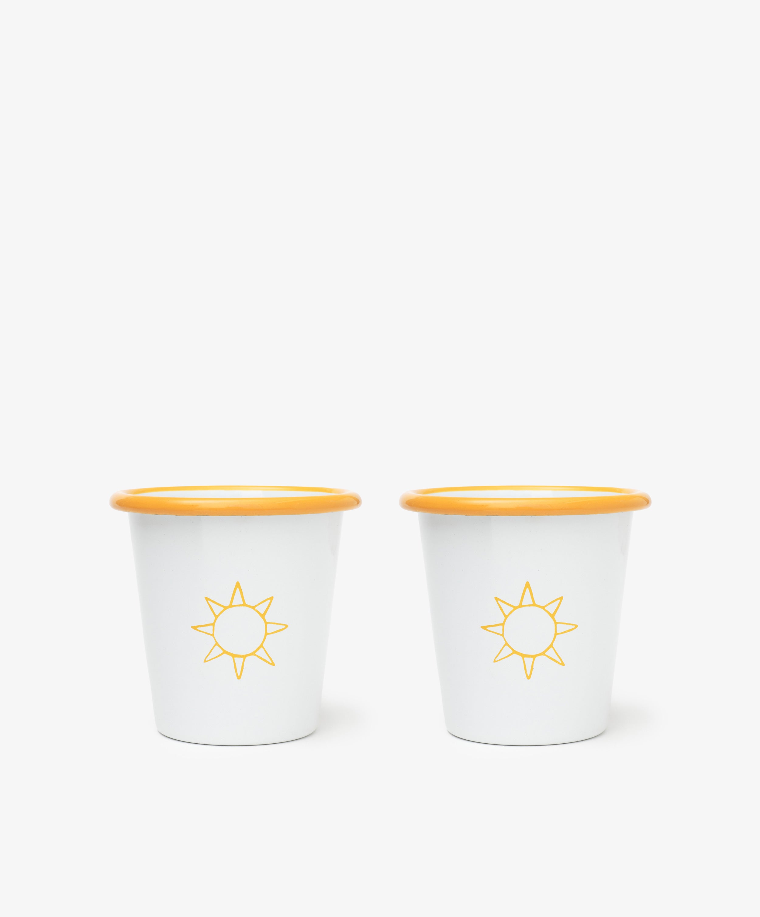 The Il Sole Enamel Cup, Set of 2, features white cups with yellow rims and sun motifs, placed side by side on a plain white background for a cheerful summer vibe.