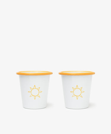 The Il Sole Enamel Cup, Set of 2, features white cups with yellow rims and sun motifs, placed side by side on a plain white background for a cheerful summer vibe.