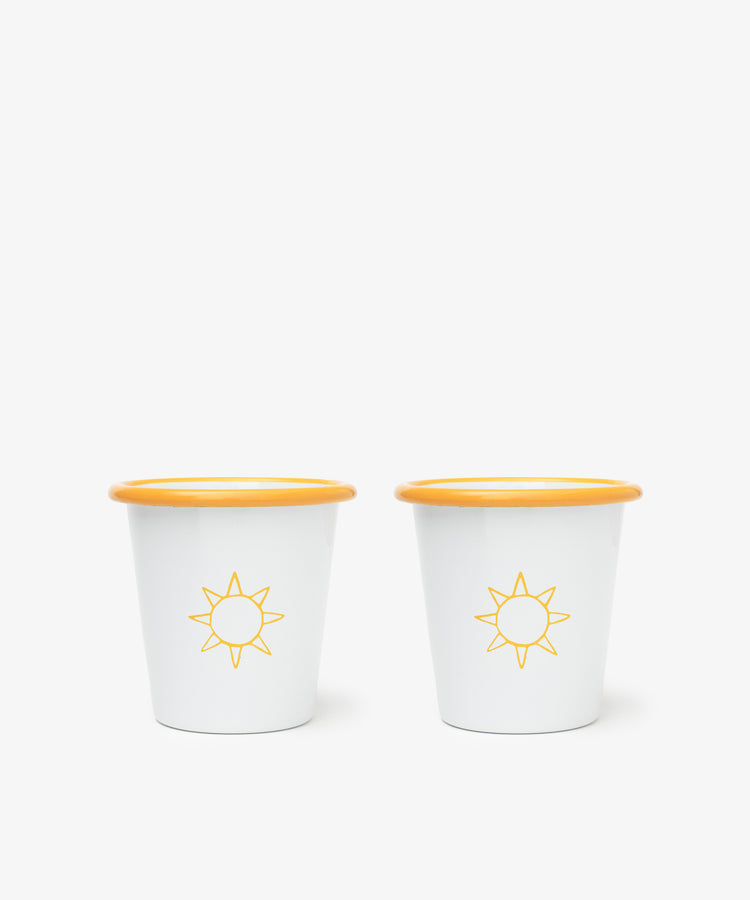 The Il Sole Enamel Cup, Set of 2, features white cups with yellow rims and sun motifs, placed side by side on a plain white background for a cheerful summer vibe.